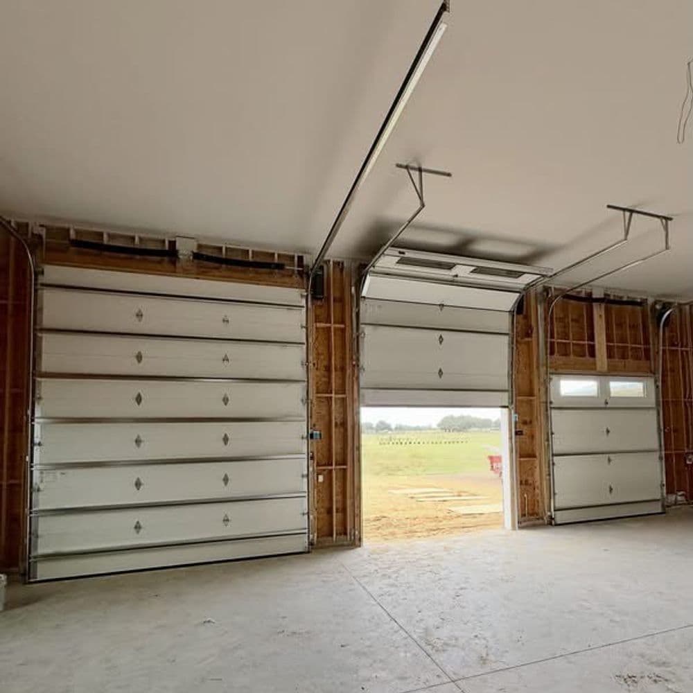 Garage interior featuring two large doors and an exit door, with unfinished walls and flooring.