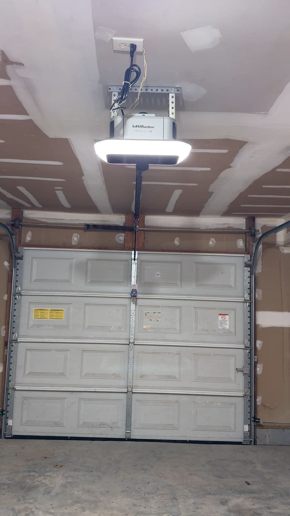 Garage door opener installed on ceiling with an illuminated lamp and unfinished drywall background.