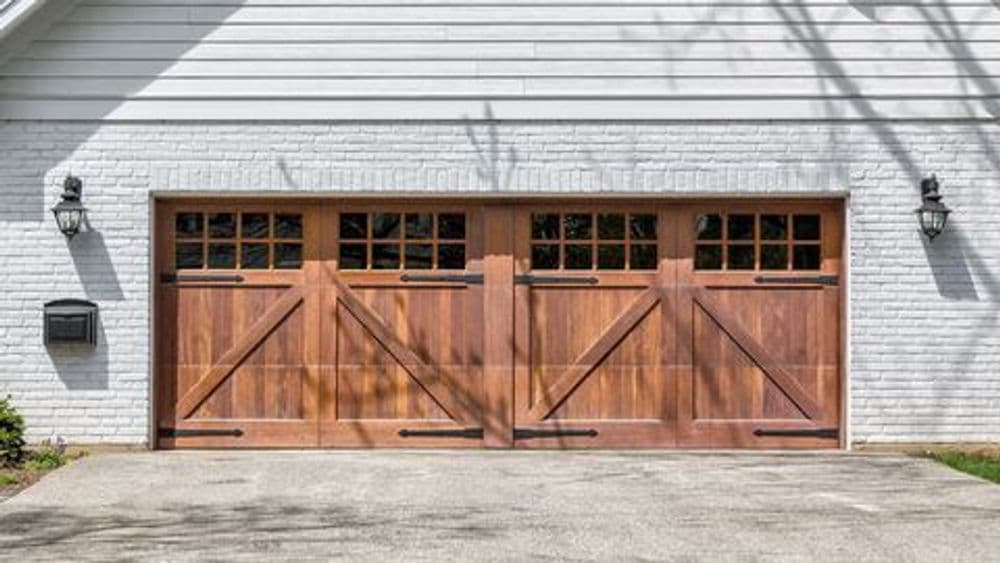 Wooden garage doors with windows on a white brick house exterior. Modern rural design.