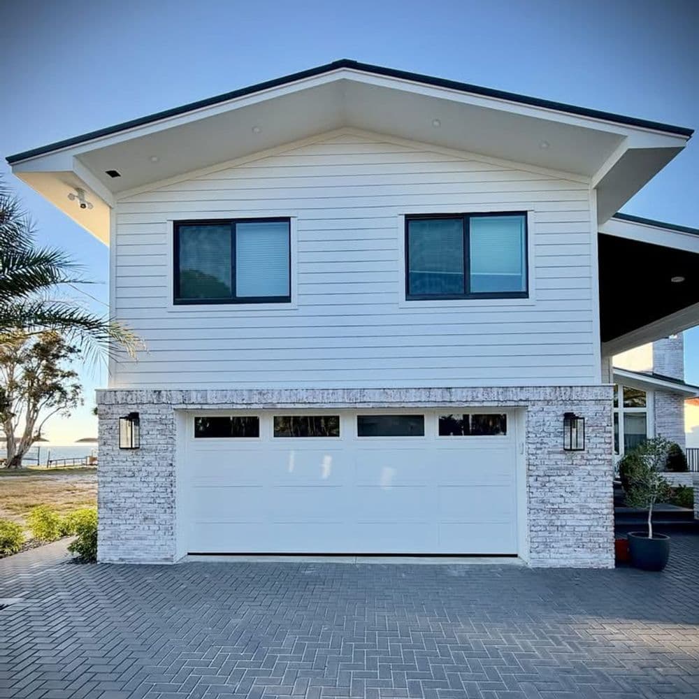 Modern waterfront house with white siding, garage, and large windows against a clear sky.