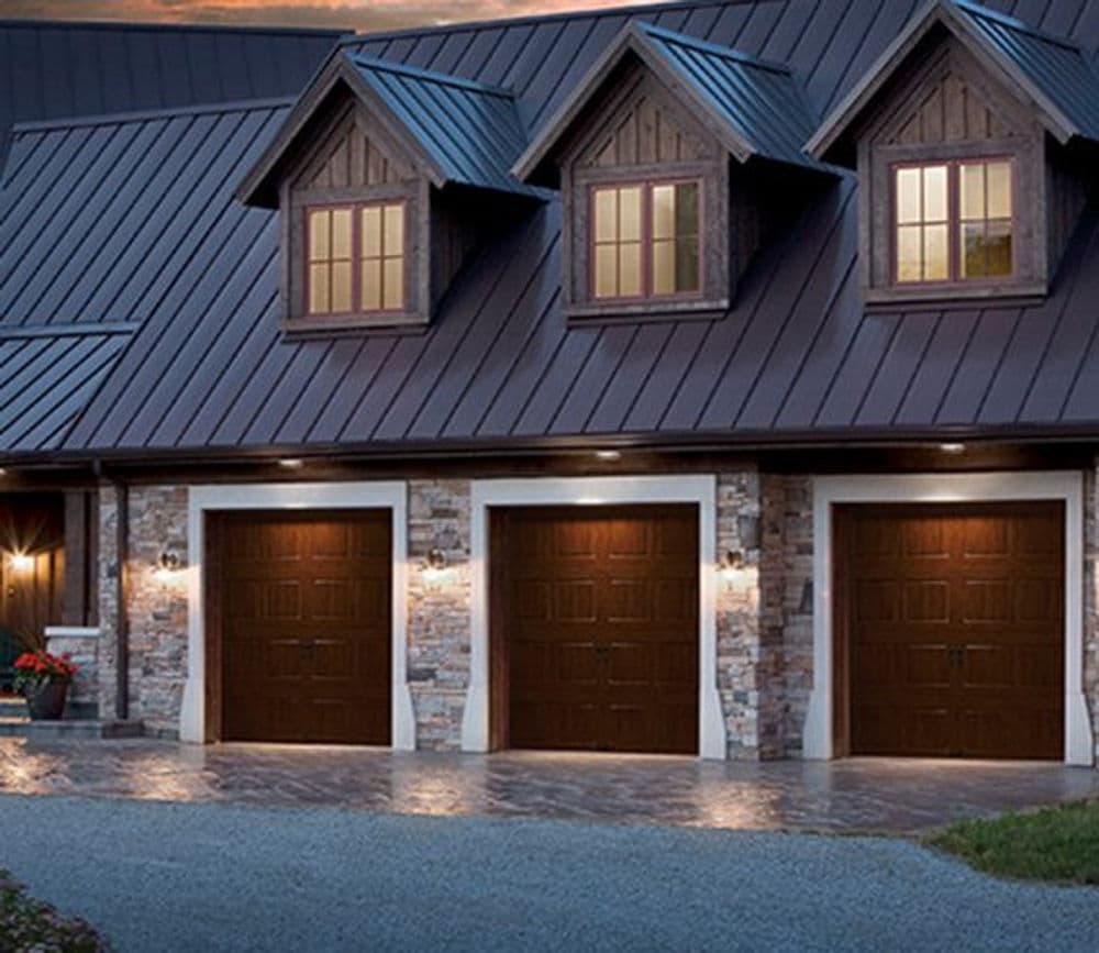 Modern home exterior with stone accents, three garage doors, and illuminated windows at dusk.
