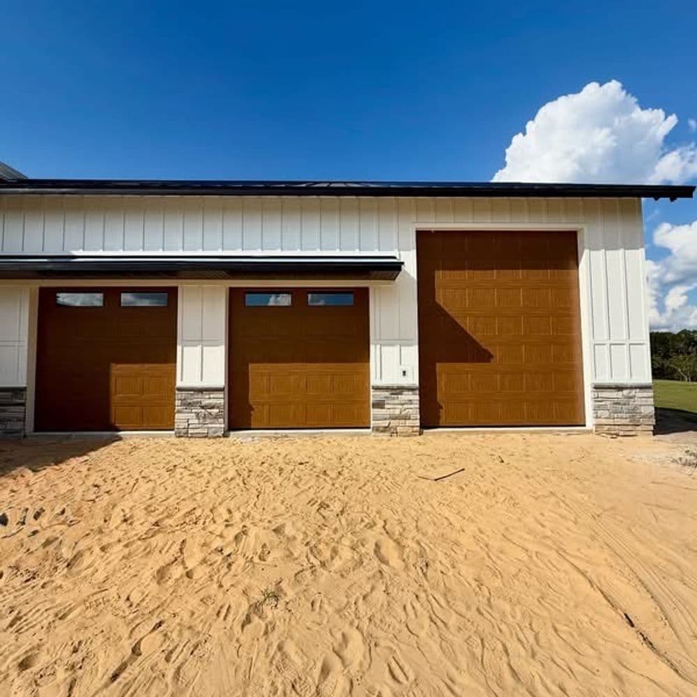 Modern garage with brown doors and stone accents against a sandy landscape and blue sky.