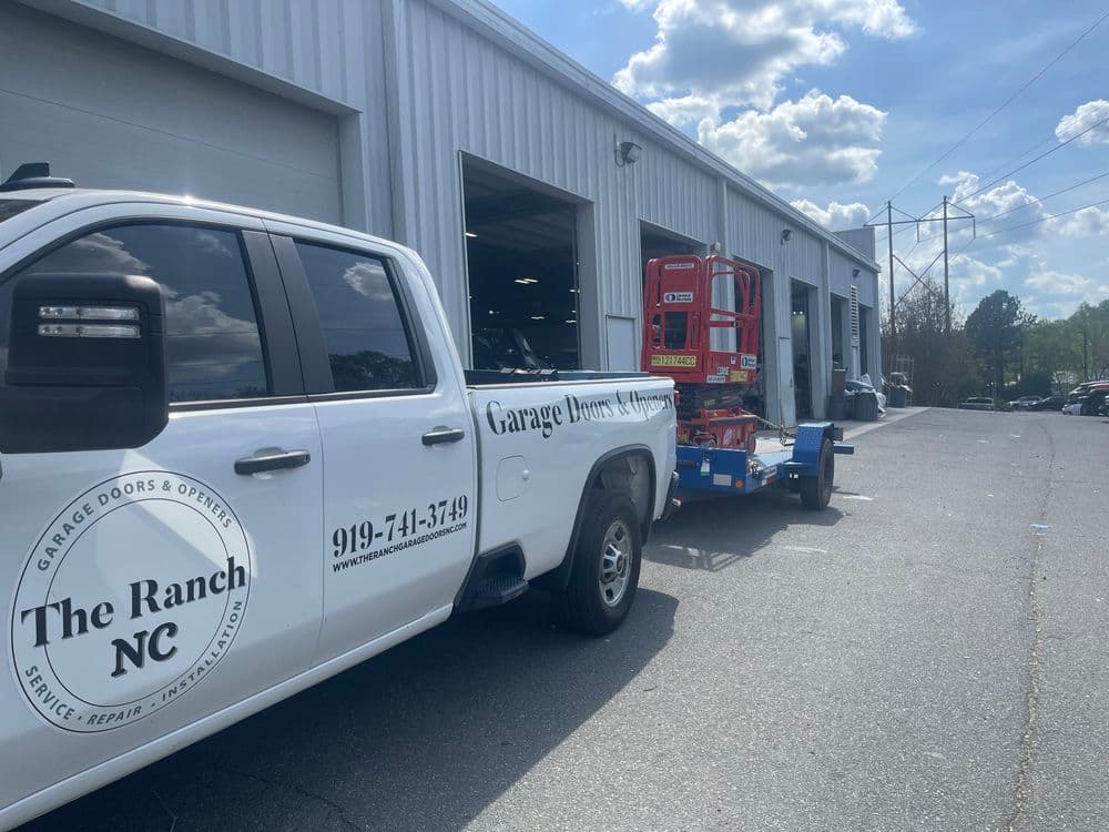 White service truck for The Ranch NC parked outside a garage with equipment trailer attached.