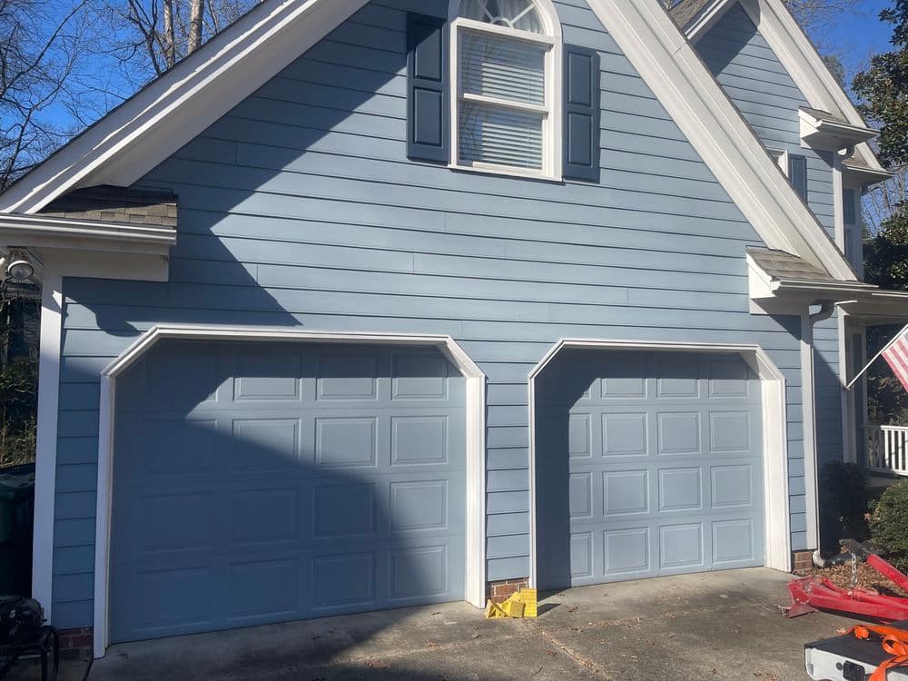 Blue house exterior with two garage doors and a white porch, showcasing a classic design.