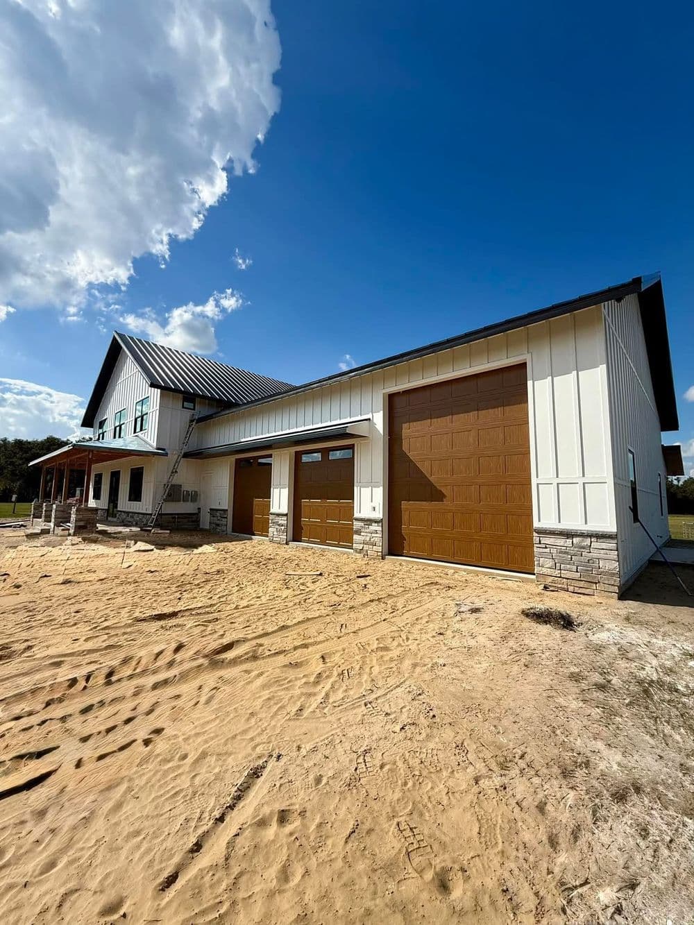 Modern farmhouse with a two-car garage, white siding, stone accents, and a blue sky backdrop.