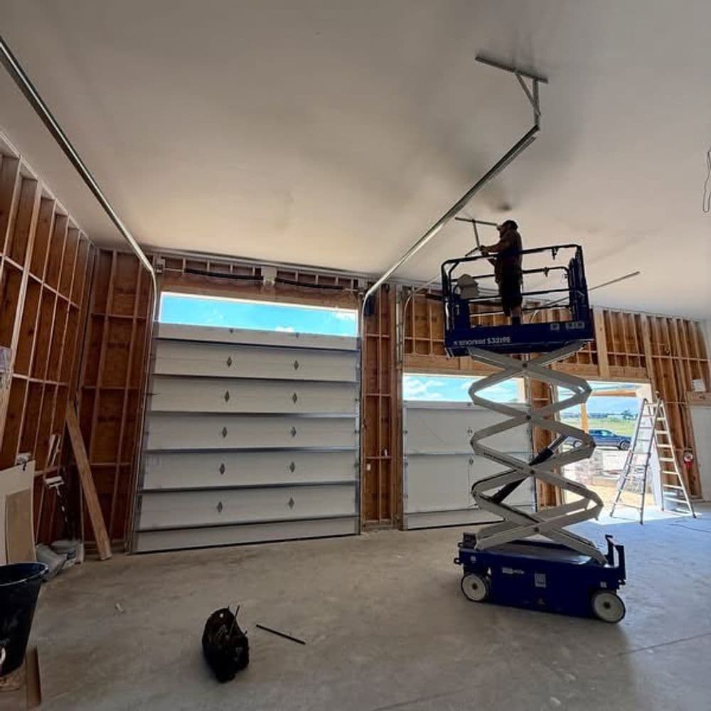 Worker using a scissor lift to install lighting in a garage under construction.
