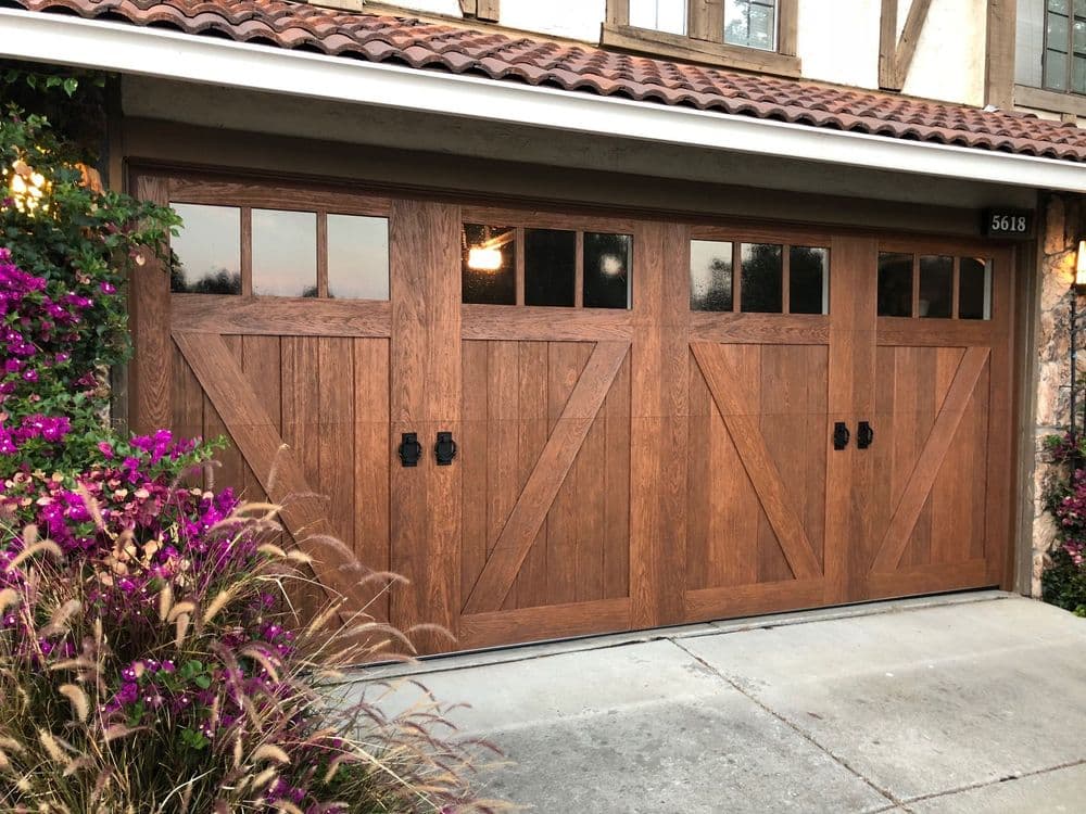 Elegant brown wooden garage door with decorative glass panels and vibrant landscaping.