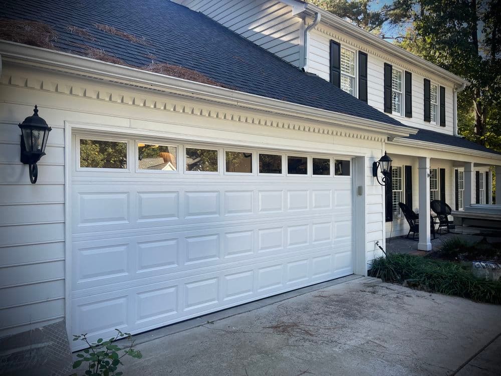 White garage door with decorative windows, modern home exterior, and landscaped driveway.