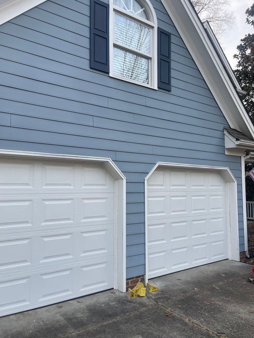 Blue house exterior with two white garage doors and decorative shutters.