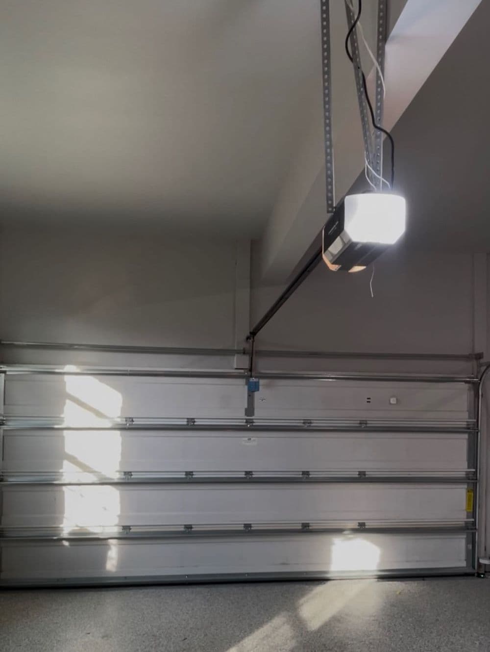 Brightly lit garage interior with a modern garage door and ceiling-mounted opener.