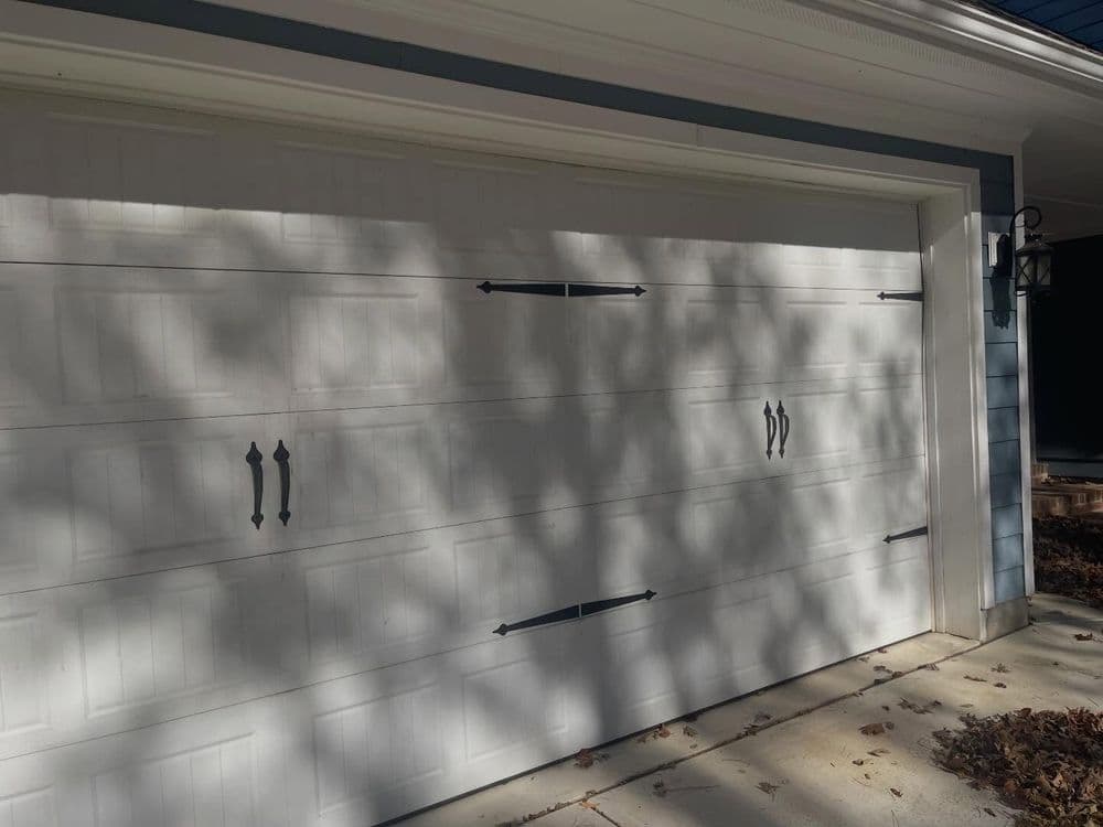 White garage door with decorative black hardware and shadows cast on the surface.