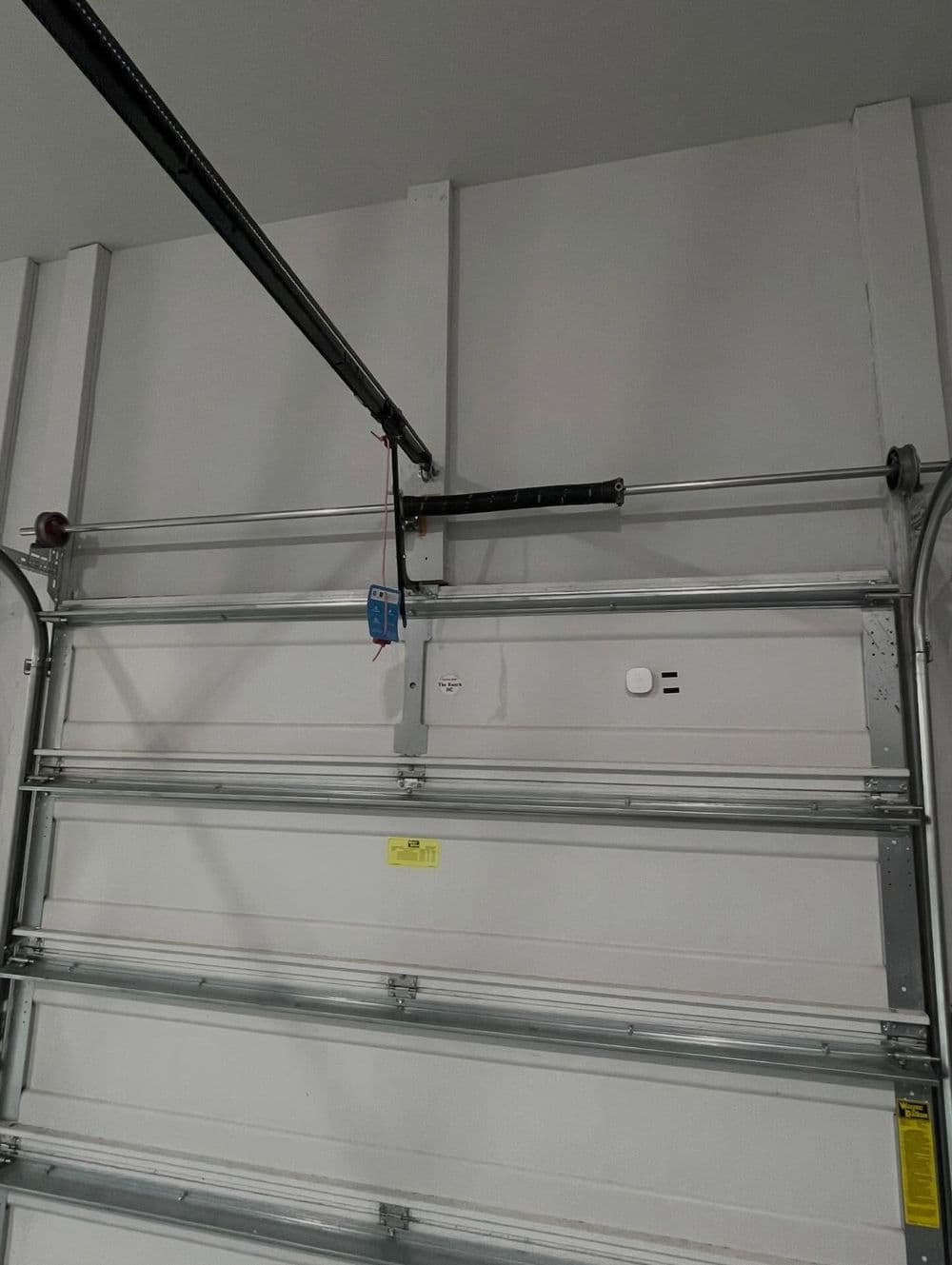 Garage door mechanism with tracks and spring system mounted on a white wall.