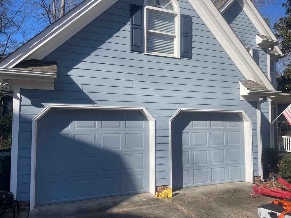 Blue house exterior featuring two garage doors and a front porch with an American flag.