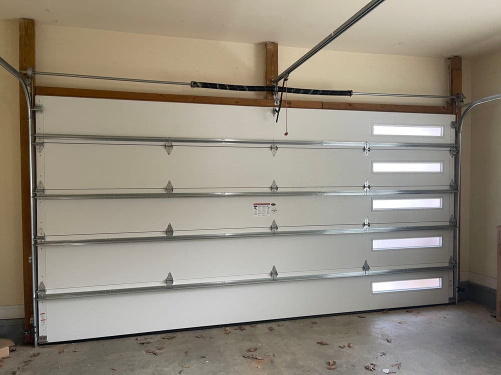Modern white garage door with windows, installed in a spacious garage.